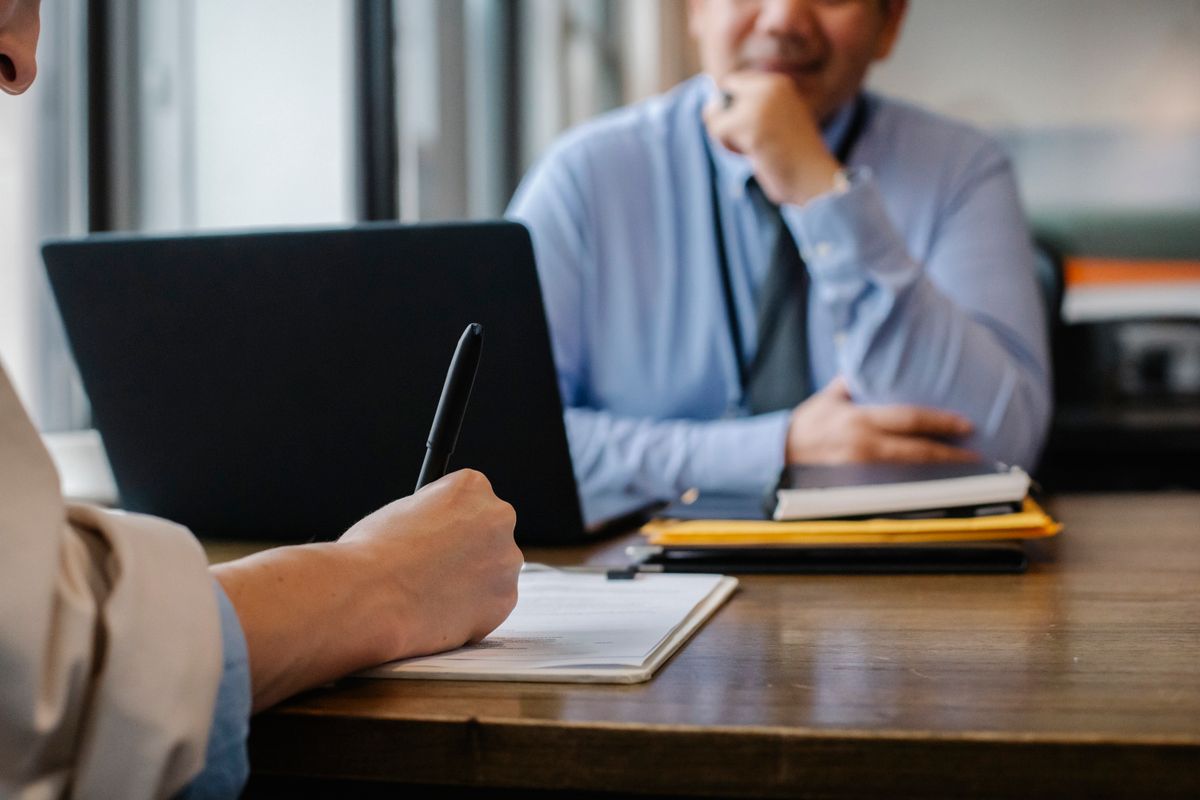 A person filling out paperwork beside a laptop — compliance procedures